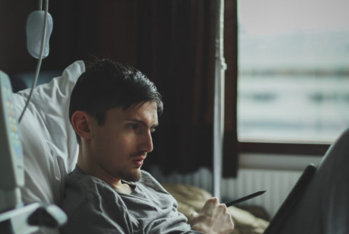 man sitting in hospital bed looking at ipad