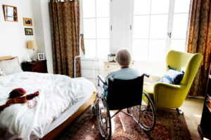 a woman sits in a wheelchair beside a bed