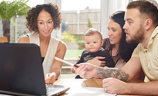 a woman helping a Family with a baby sitting at table looking at laptop