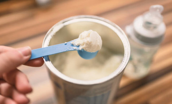 a person holding a scoop of baby formula over a baby formula can