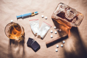 drugs on a table including alcohol, pills, a syringe, and baggies of powder