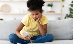 a young girl sits looking at her phone, appearing bored
