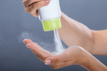 A person squeezes a container of talcum powder for use