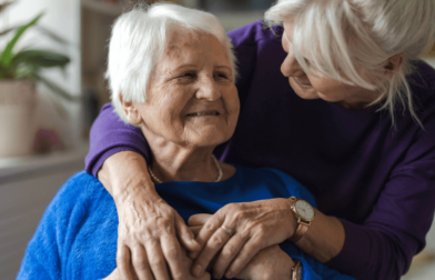 A woman puts her arms around a smiling nursing home resident