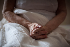 An older resident clasps their hands in their lap